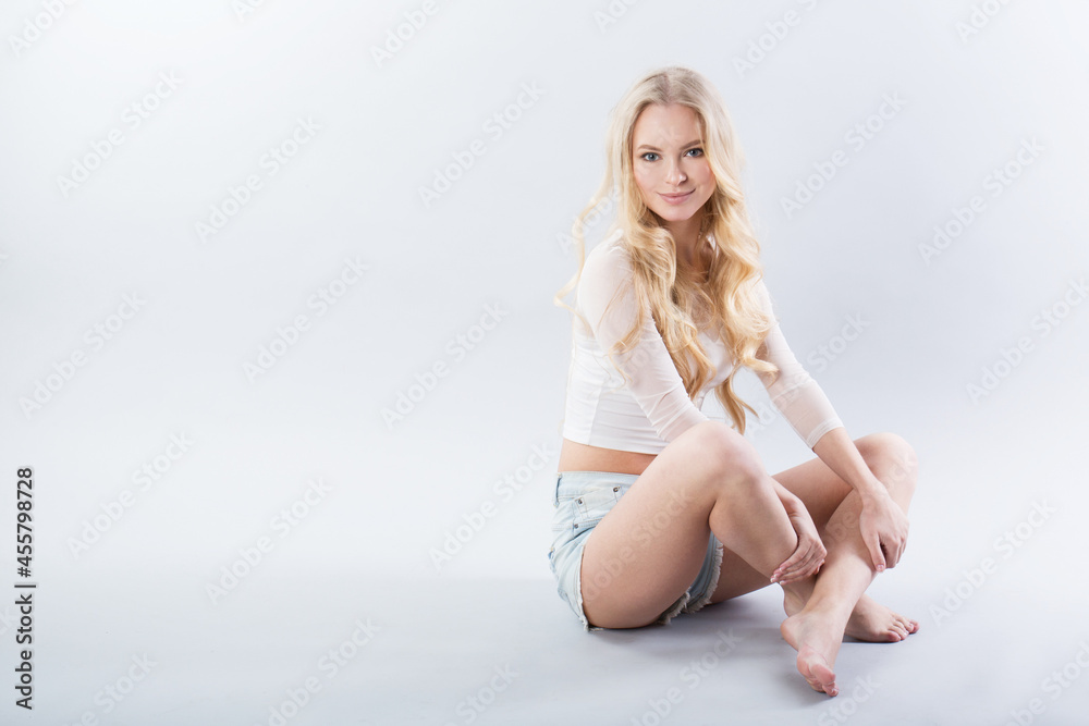 Beautiful smiling blonde in denim shorts sits on a white Beautiful smiling blonde in denim shorts sits on a white