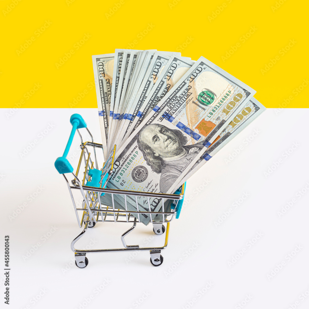 Toy supermarket cart or shopping trolley full of money isolated on yellow and white background. Money loan or sale concept