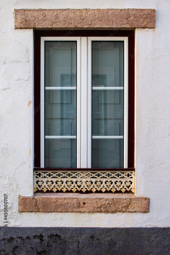 Restored traditional old window in Portuguese neighborhood with white and red frame and carved metal guard