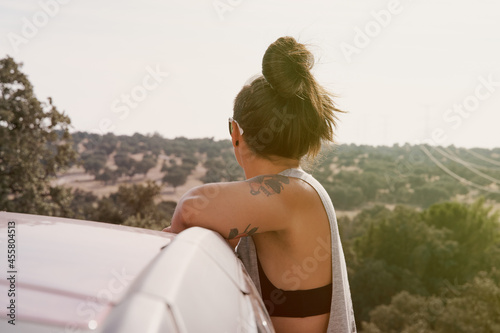 Rear view of a woman enjoying herself in a car in a field at sunset.