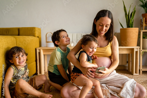 Pregnant mother using the phone with her children photo