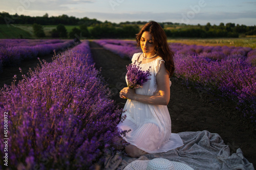 beautiful slim bride in luxurious wedding dress in purple lavender flowers. Fashion romantic stylish happy woman with blond hair. Smiling girl in sunset over summer lavenda waiting for groom -Provence
