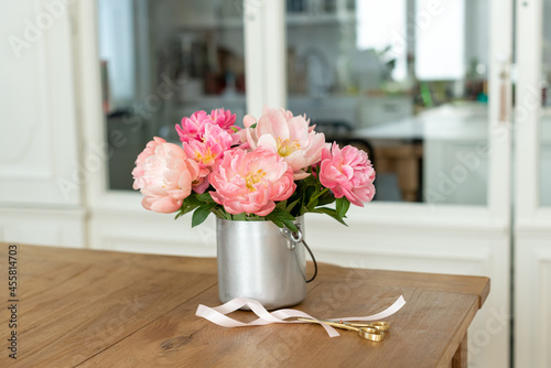 Fototapeta Naklejka Na Ścianę i Meble -  Closeup of a bouquet of pink peonies in a metal vase on the table with scissors and a ribbon on it