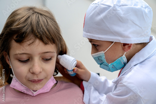 Little brother playing doctor checking ear of little sister with otoscope