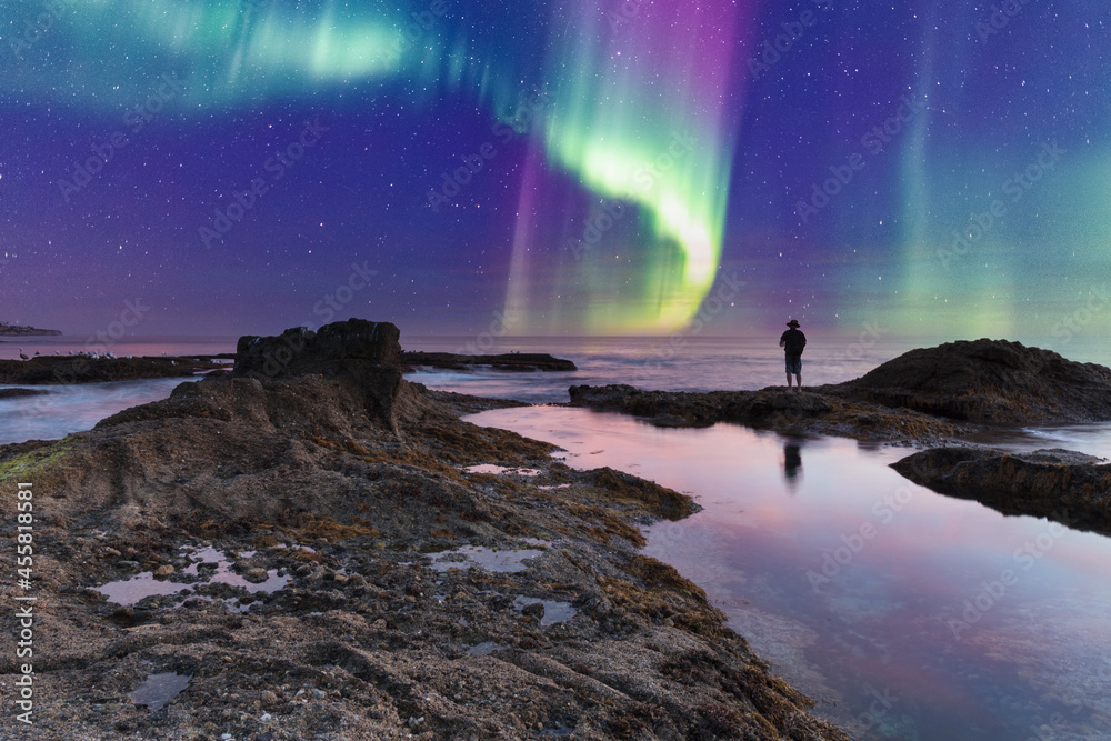 Man’s reflection silhouette as a Green Aurora borealis shimmers over the ocean water - obrazy, fototapety, plakaty 