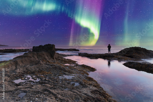 Man’s reflection silhouette as a Green Aurora borealis shimmers over the ocean water