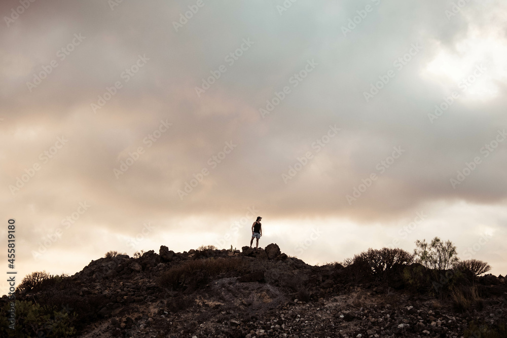 Silueta de persona encima de una montaña con el atardecer y nubes de fondo detrás