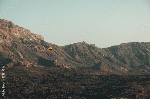 Helicóptero de emergencias sobrevolando un paisaje rocoso y desértico de una isla volcánica