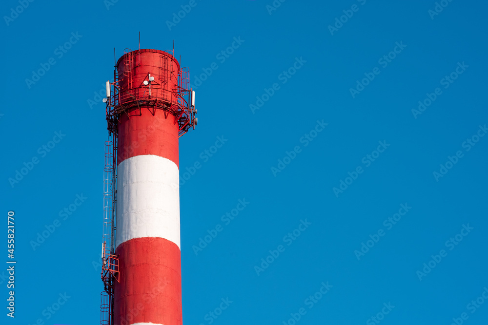 top of an industrial chimney with antennas attached to it against a blue sky