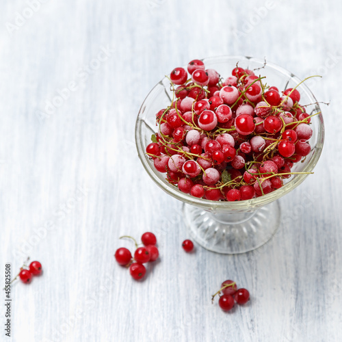Frozen red currants in a glass vase on a white wooden table. Close-up.