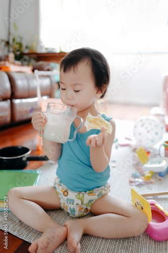 Asian baby sitting on the ground eating breakfast and drinking milk