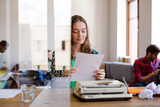 Creative businesswoman reviewing paperwork at typewriter in office
