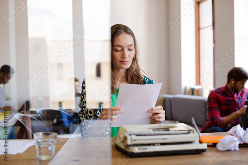 Creative businesswoman reviewing paperwork at typewriter in office