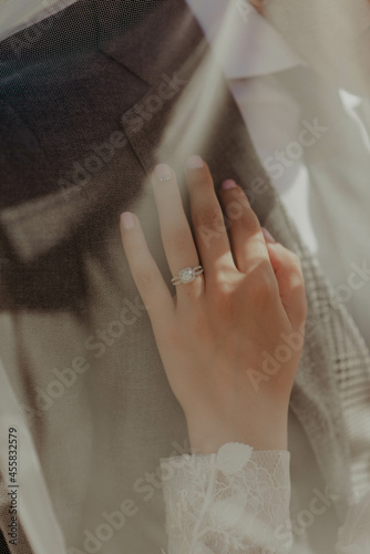 Bride's hand with engagement ring on her finger touching her groom's garment photo