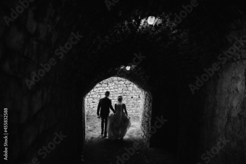 Fotografija Grayscale shot of the bride and groom walking in the tunnel of a fortress