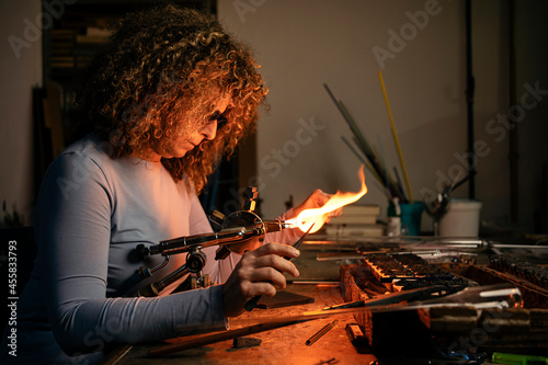 Side view of woman lampworker working with glass tubes with the torch flame photo