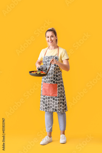 Young housewife with tasty dish in frying pan on color background