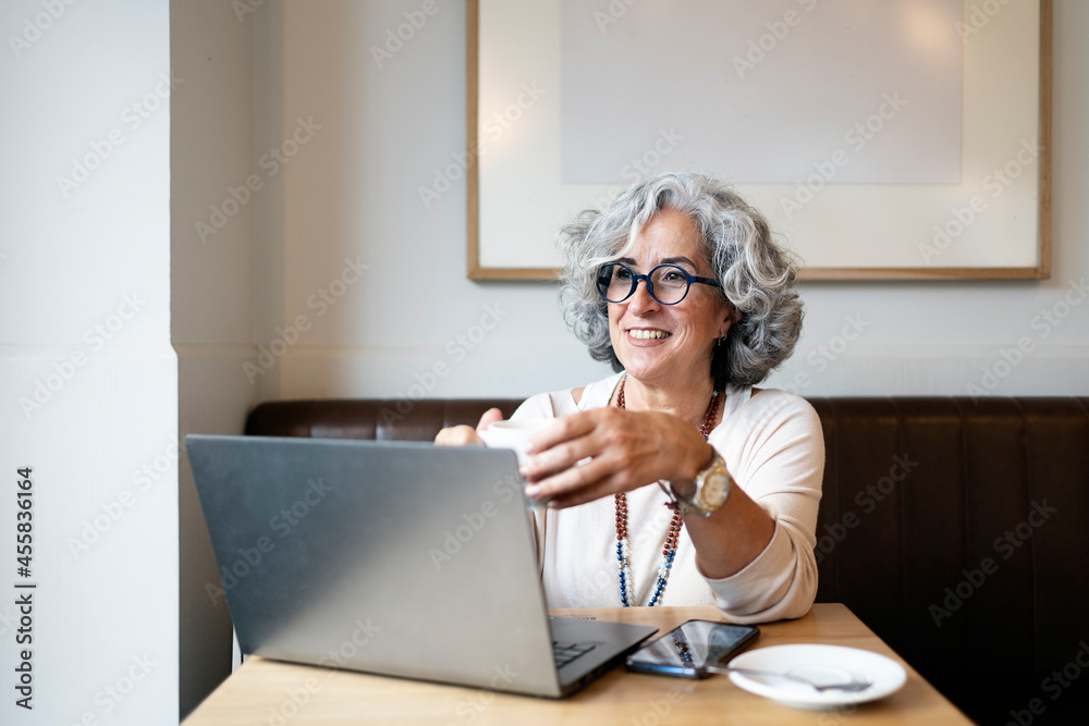 Mature woman using laptop and drinking coffee in a cafe Mature woman using laptop and drinking coffee in a cafe