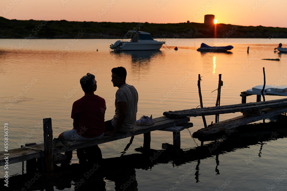 Gay couple sitting on a pier at dusk Gay couple sitting on a pier at dusk