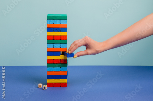 Tower of colorful blocks on blue paper background with hand touching it