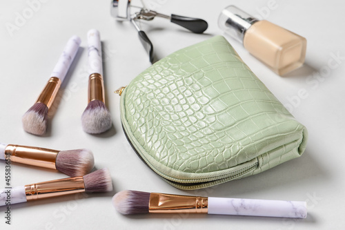Stylish cosmetic bag, brushes, makeup foundation and eyelash curler on light background, closeup