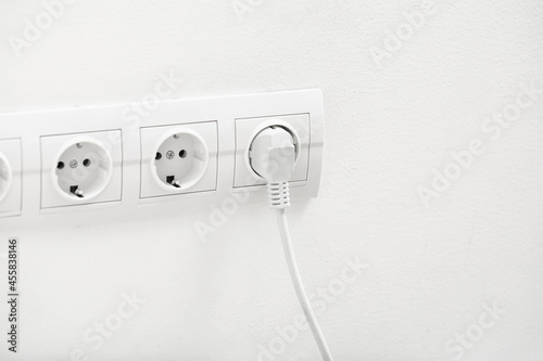 Electric socket with plug on light wall photo