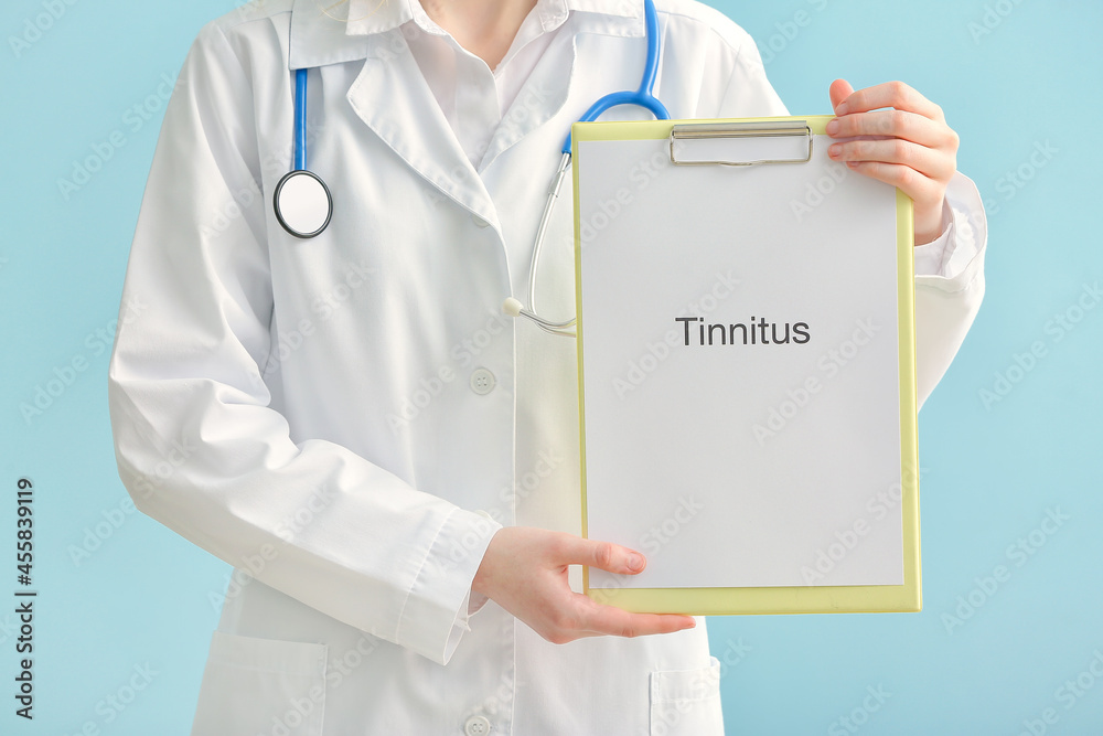 Female doctor holding clipboard with word TINNITUS on color background Female doctor holding clipboard with word TINNITUS on color background