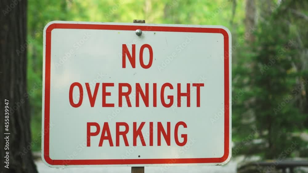 No overnight parking sign in Glacier NP Campground and Creek with green trees in the background. No overnight parking sign in Glacier NP Campground and Creek with green trees in the background.