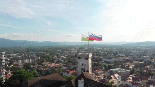 Slow drone flying up with a view of Ljubljana city above the castle with the flag of the city and a national Slovenian flag photo