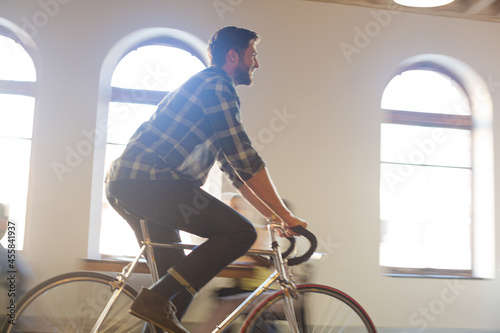 Casual businessman riding bicycle in sunny office
