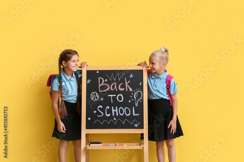 Cute pupils near chalkboard on color background