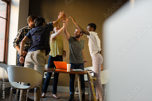 Casual business people raising hands in circle in sunny office meeting