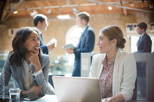 Businesswomen talking and working at laptop in office