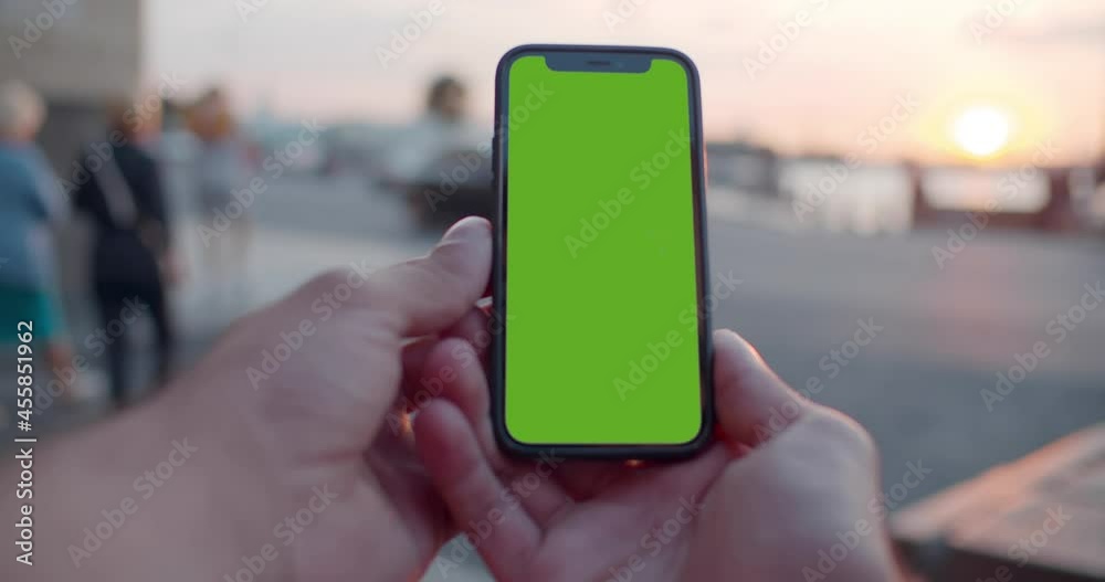 Pov bokeh shot of man hands holding modern black mobile phone with blank green screen.