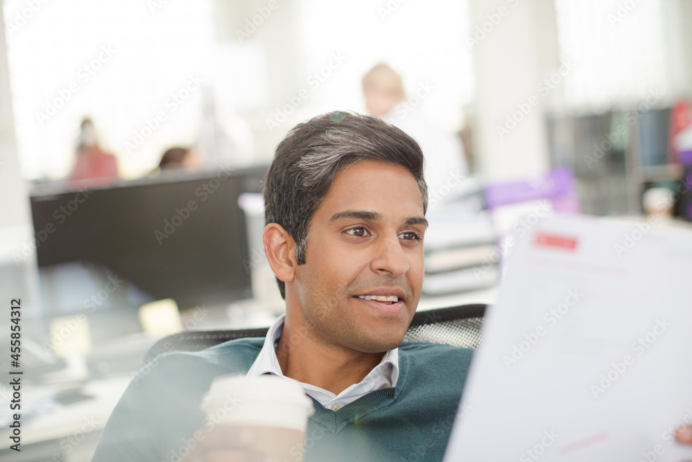 Smiling businessman drinking coffee and reviewing paperwork