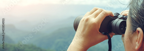 Young girl looks through binoculars on mountains background photo
