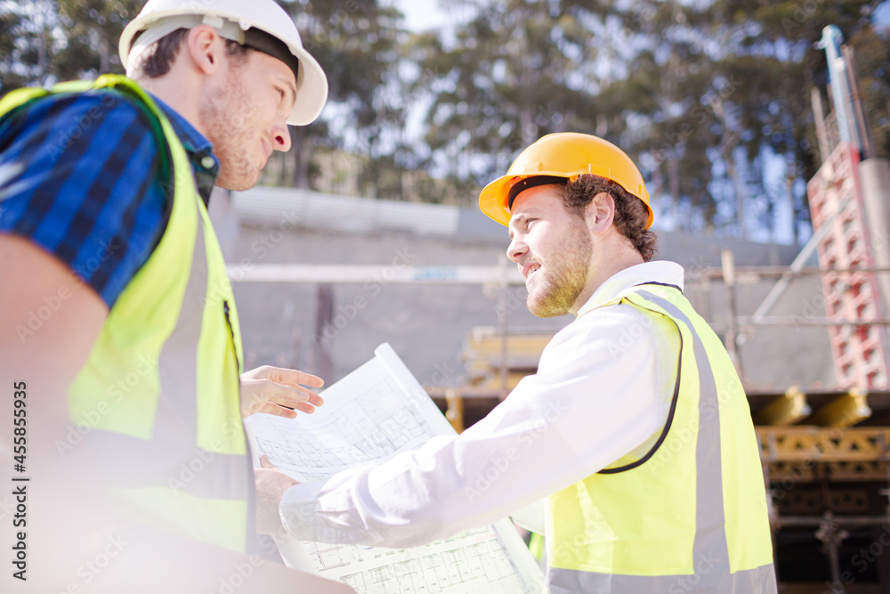Construction worker engineer reviewing blueprints below crane at construction site Construction worker engineer reviewing blueprints below crane at construction site