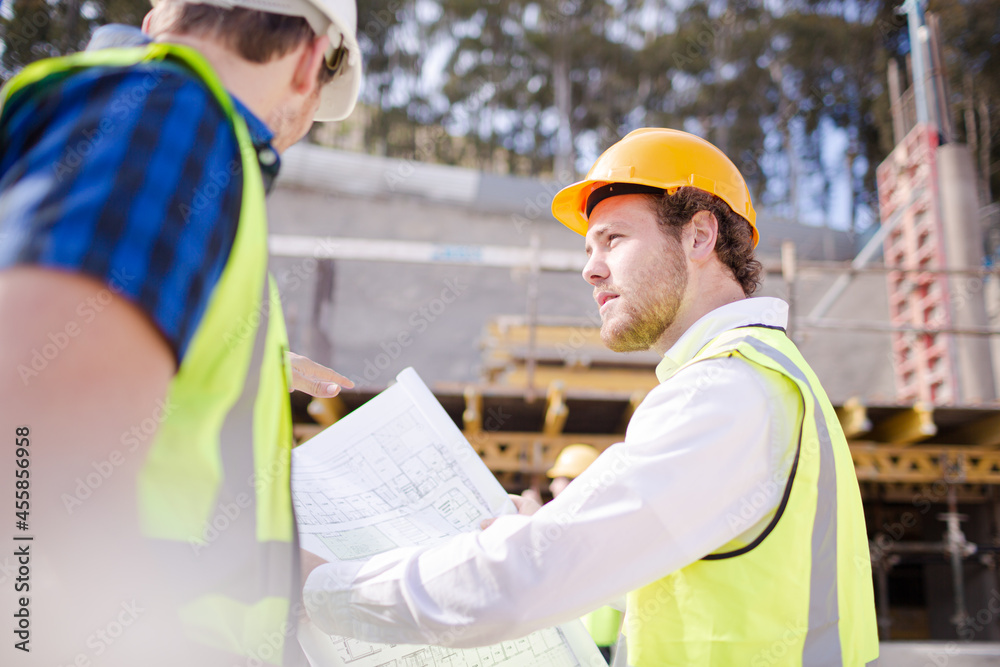 Construction worker engineer reviewing blueprints below crane at construction site