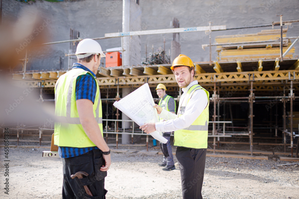 Construction worker engineer reviewing blueprints below crane at construction site Construction worker engineer reviewing blueprints below crane at construction site