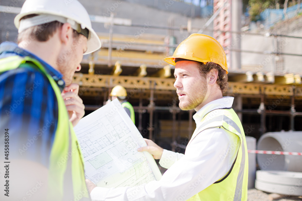 Construction worker engineer reviewing blueprints below crane at construction site Construction worker engineer reviewing blueprints below crane at construction site