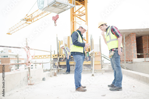 Foreman talking to construction worker below crane at construction site