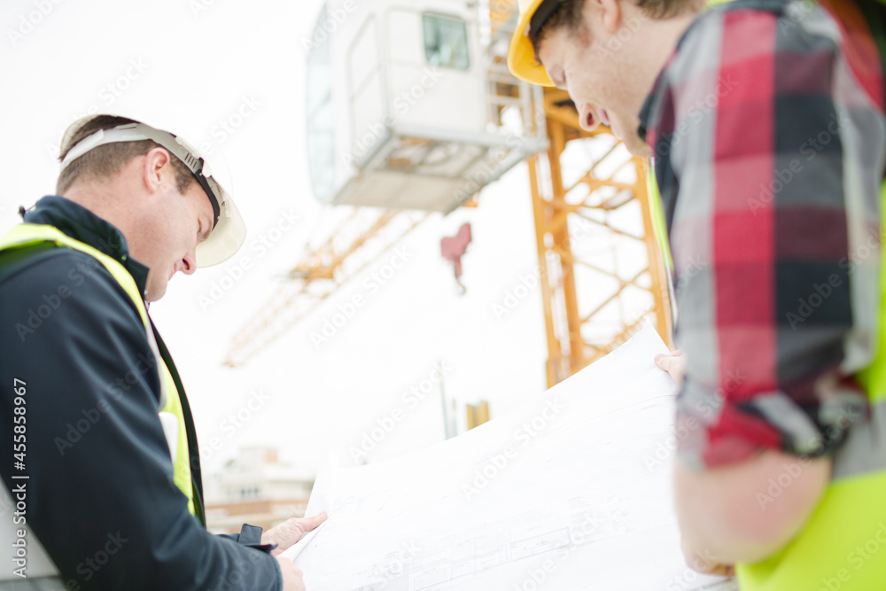 Foreman talking to construction worker below crane at construction site Foreman talking to construction worker below crane at construction site