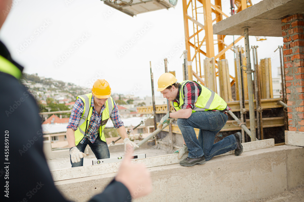 Construction workers using level tool below crane at construction site ...