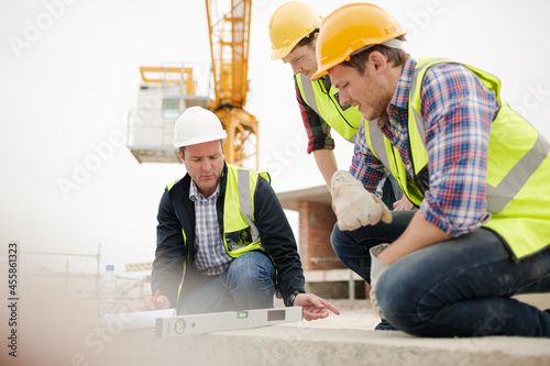 Construction workers using level tool below crane at construction site photo