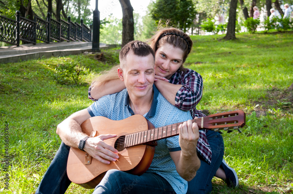 Young couple on the grass in the park in the summer, a guy plays the guitar for a girl