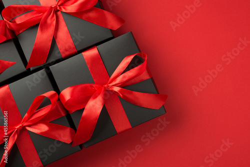 Top view photo of black gift boxes with red ribbon bow on isolated red background with copyspace
