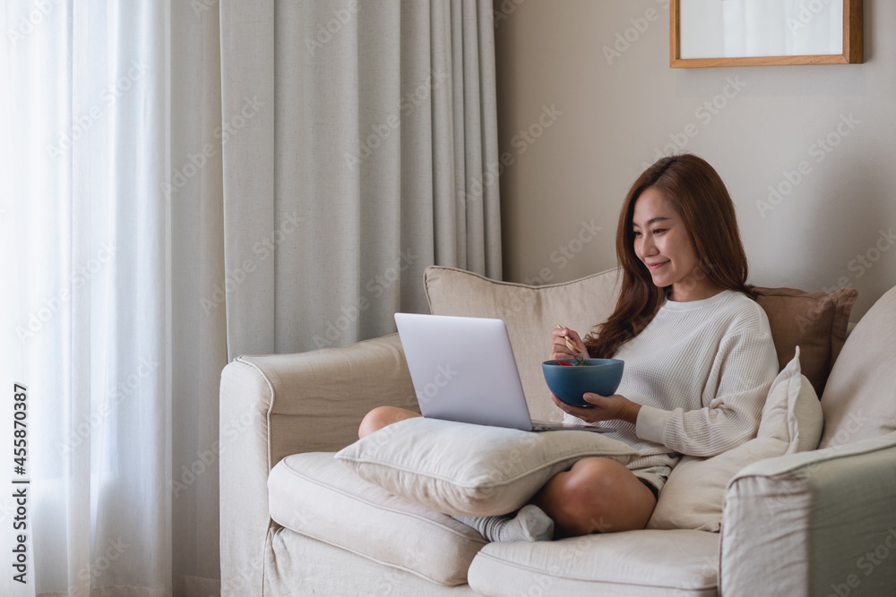A young woman eating food while using laptop computer for online working, studying, watching movie at home A young woman eating food while using laptop computer for online working, studying, watching movie at home