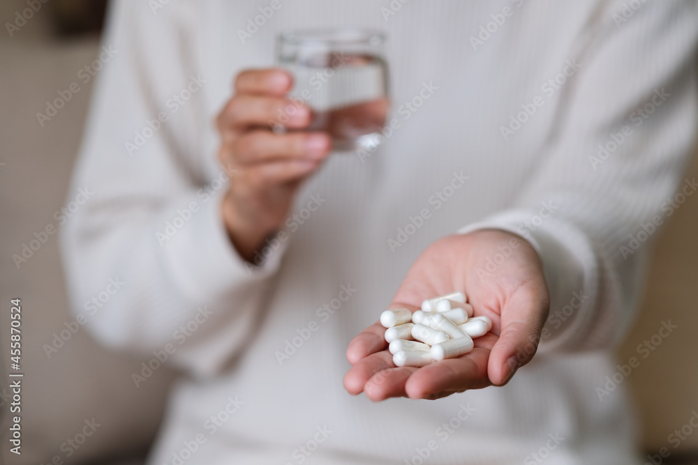 Closeup image of a woman holding white pills and a glass of water Closeup image of a woman holding white pills and a glass of water