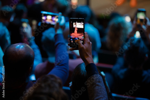 Audience members with smart phones videoing speaker on stage at conference