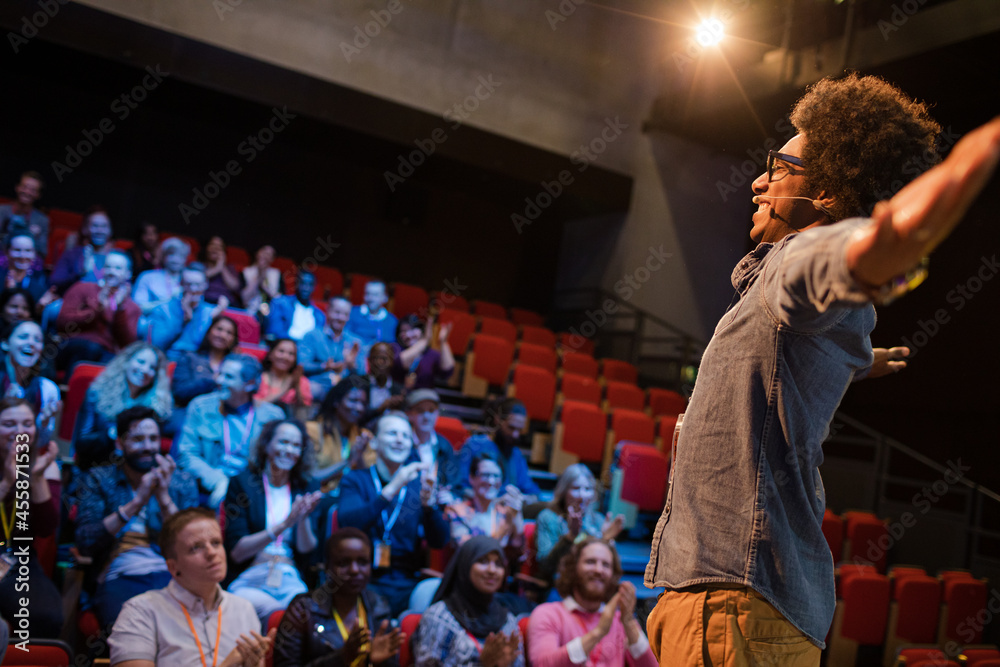 Audience watching male speaker with arms outstretched on stage Audience watching male speaker with arms outstretched on stage